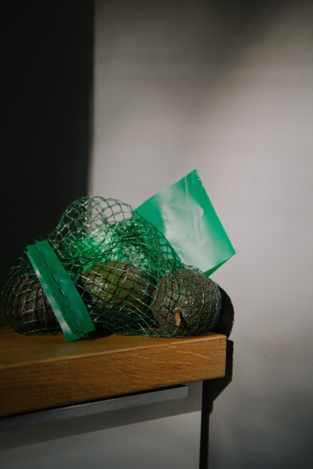Photo of avocados in a mesh bag on a wooden table