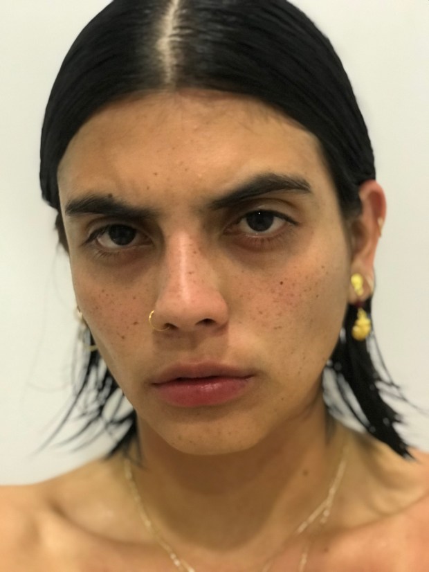 Photo of the artist with slicked shoulder length hair and bare shoulders.