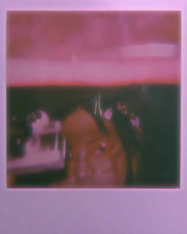 Blurry pink washed polaroid of a person's face holding a camera