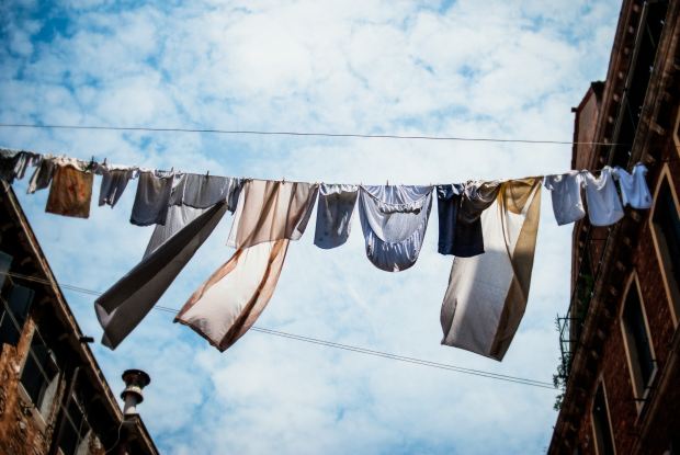 Photo of clothes on a washing line between two buildings with a blue clouded sky in the background