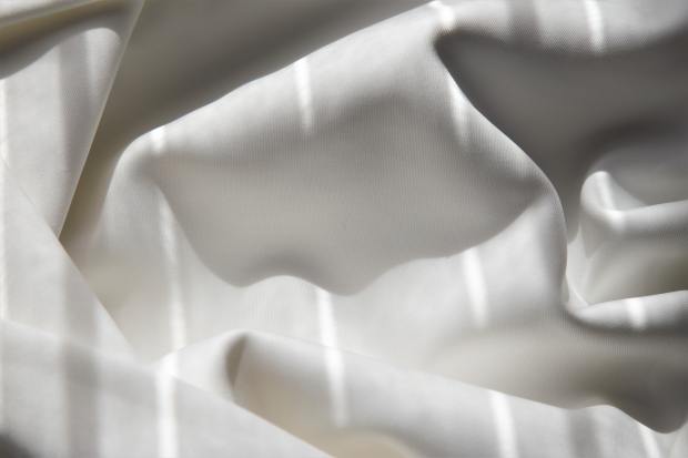 Rumpled white bedsheet splashed with lines of light