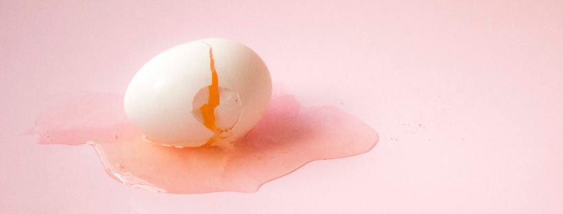 Photo of a cracked egg on a light pink backdrop
