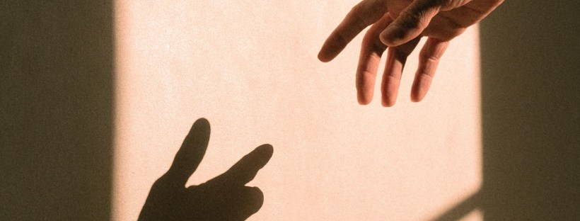 Photo of a hand in front of a sunlight wall, seemingly reaching for the shadowed hand their fleshy hand casts.