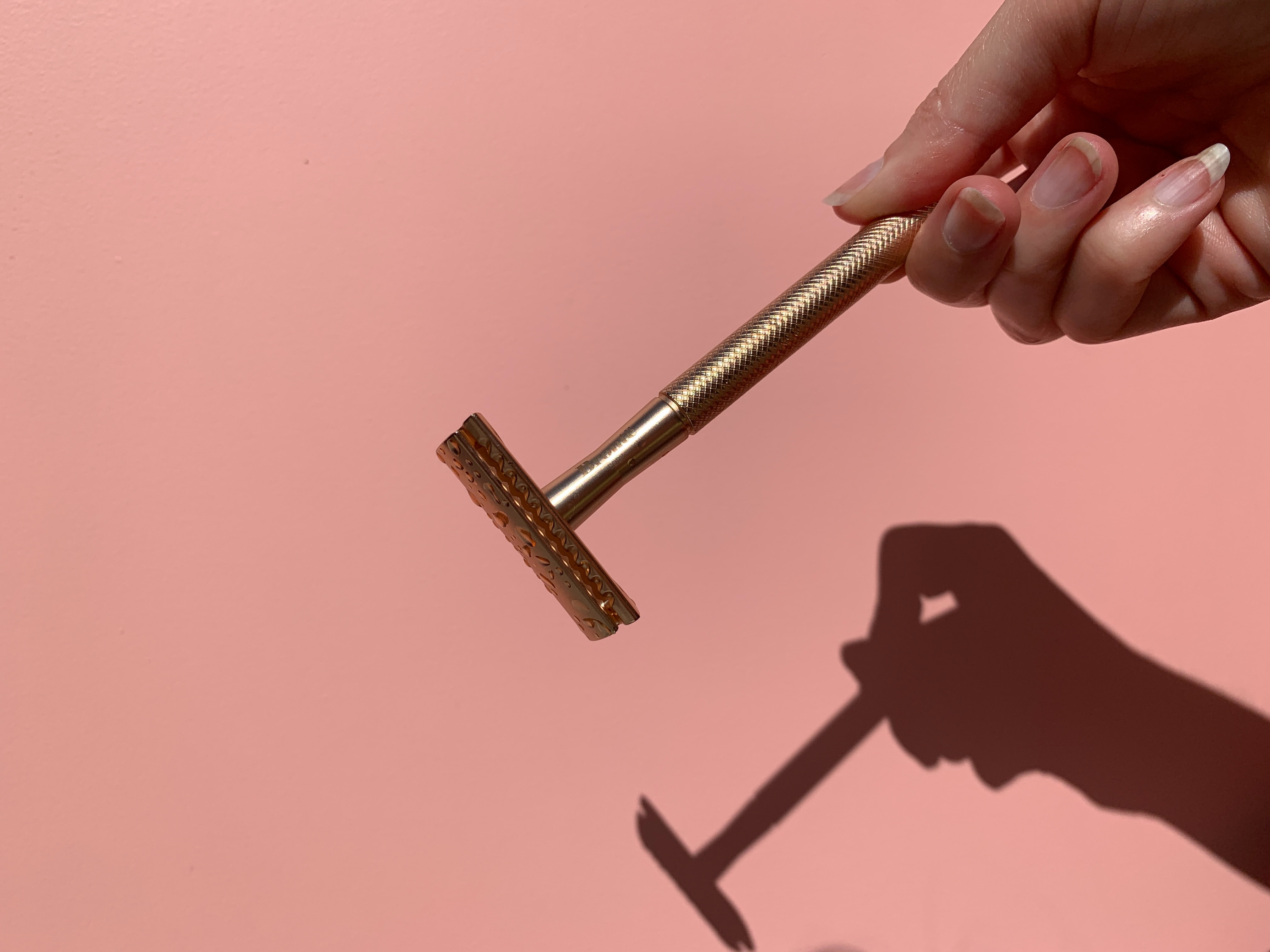 Photo of a razor in a person's hand casting a shadow on a pink background.