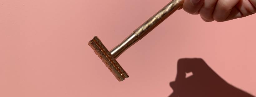 Photo of a razor in a person's hand casting a shadow on a pink background.