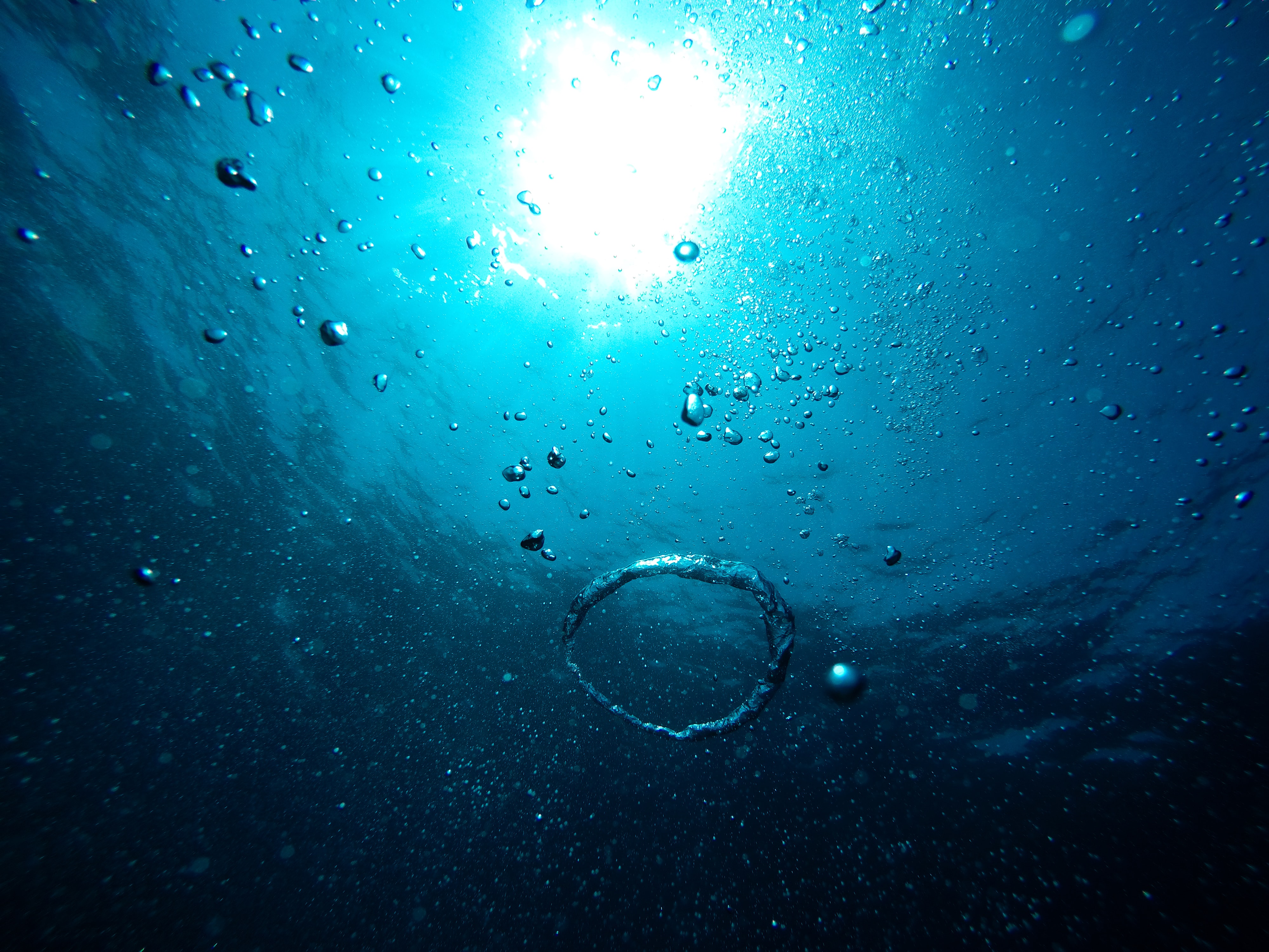 Underwater photo of blue sea with bubbles and a bright light shining above the surface.