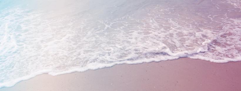 Photo of waves on a seashore with blue and pink hues.