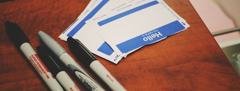 Photo of Sharpie markers and ‘Hello my name is’ stickers on a brown wood table.