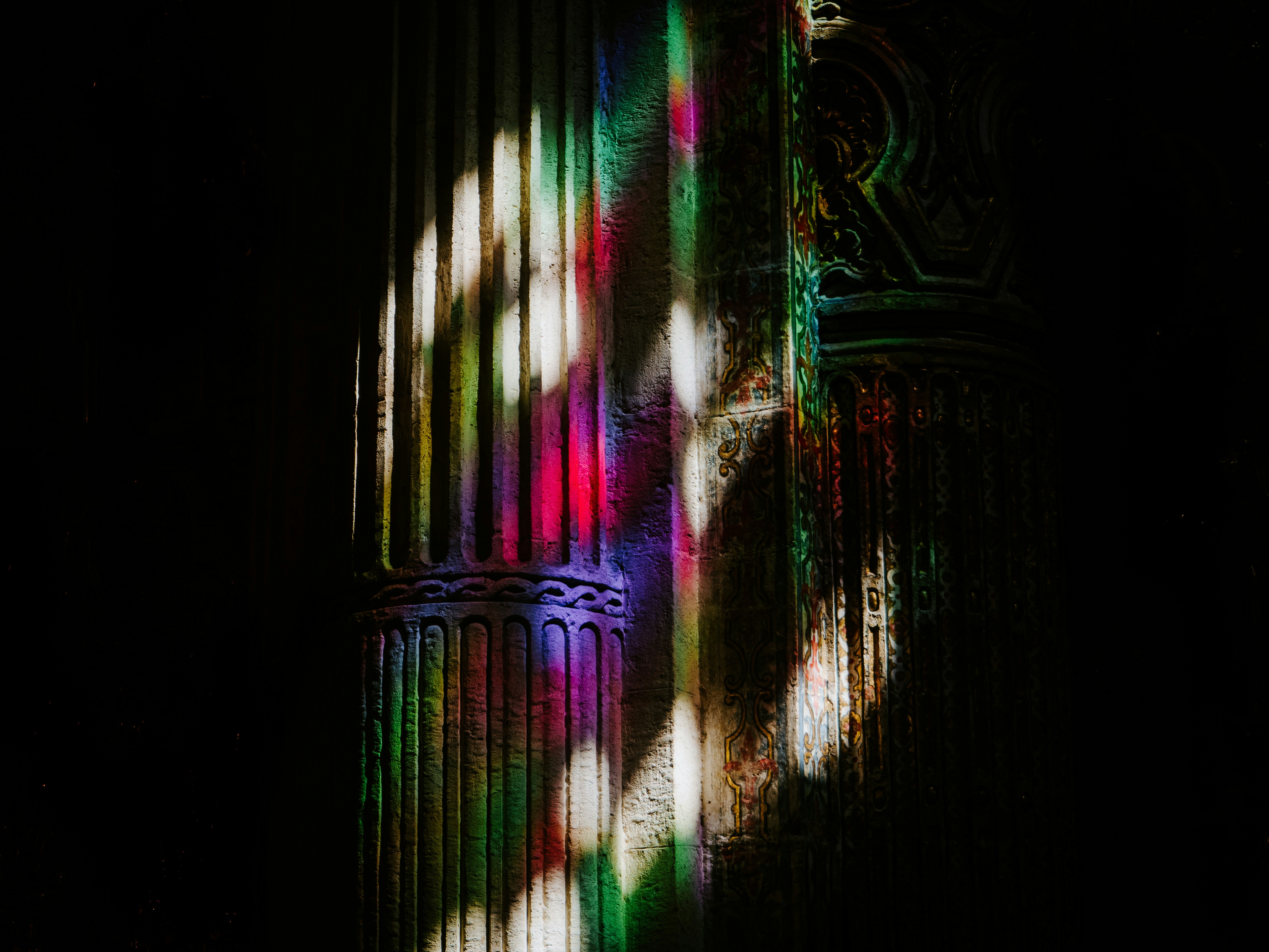 A cast of rainbow light through the stained glass of the dark Iglesia del Divino Salvador in Seville.