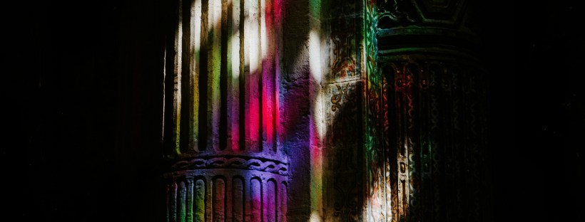 A cast of rainbow light through the stained glass of the dark Iglesia del Divino Salvador in Seville.