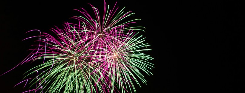 Photo of green and pink fireworks in the dark night sky.