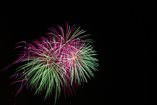 Photo of green and pink fireworks in the dark night sky.