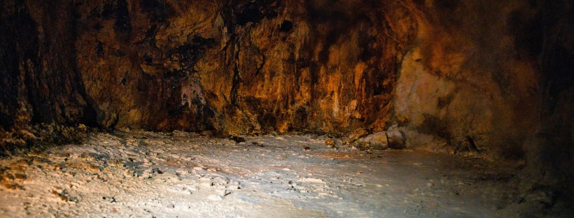 Photo of an underground cave with orange-brown rock walls and beige floor.