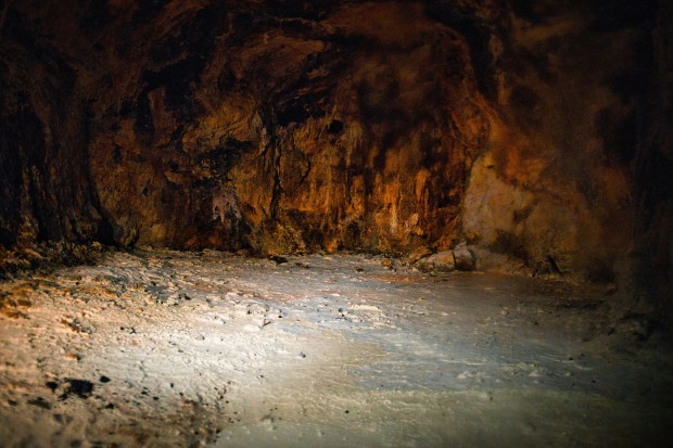 Photo of an underground cave with orange-brown rock walls and beige floor.