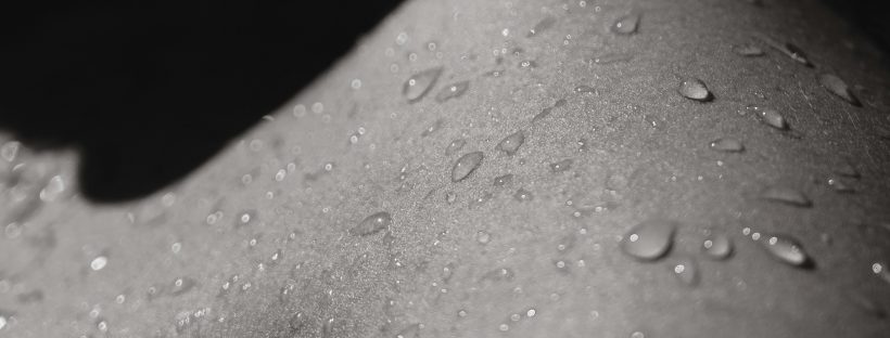 Black and white shadowed photo of a person's skin flecked with droplets of water.