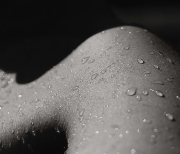 Black and white shadowed photo of a person's skin flecked with droplets of water.
