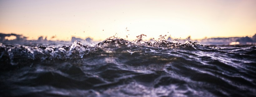 Close up photo of dark ocean waves with a sunset backdrop.