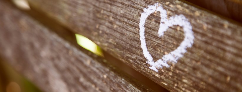 Photo of a painted white heart on the back of a wooden park bench.