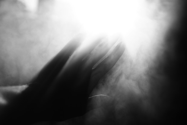 Black and white photo of a hand reaching towards bright light through smoke.
