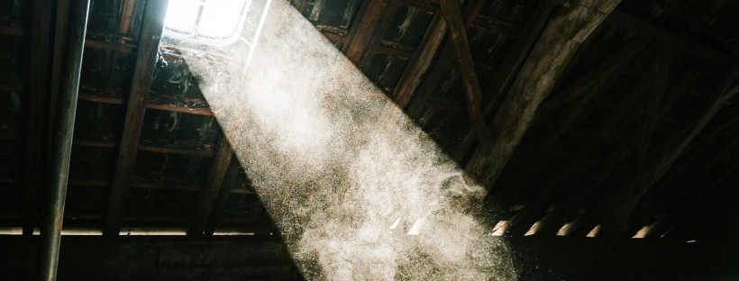 Photo of light streaming through an attic window. The attic has large wooden beams
