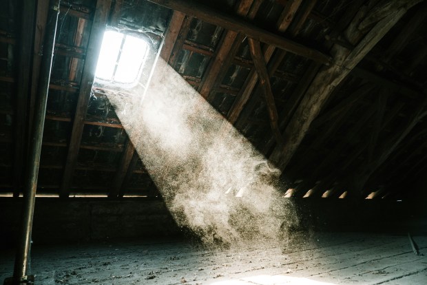 Photo of light streaming through an attic window, illuminating dust in the air. The attic has large wooden beams and dusty floorboards.