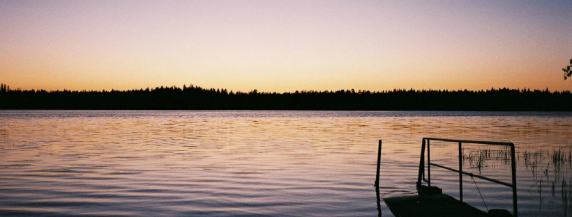 A small boat sitting on a calm lake at sunset, the colours of blue and gold.
