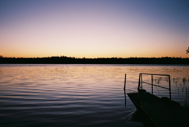 A small boat sitting on a calm lake at sunset, the colours of blue and gold.