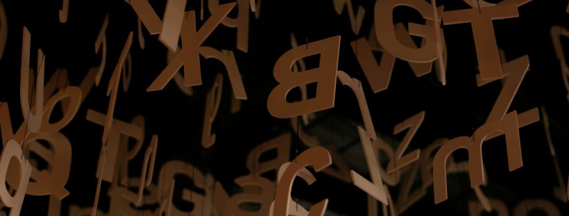 Photo of cardboard upper and lower case letters hanging from the ceiling in a dark room.