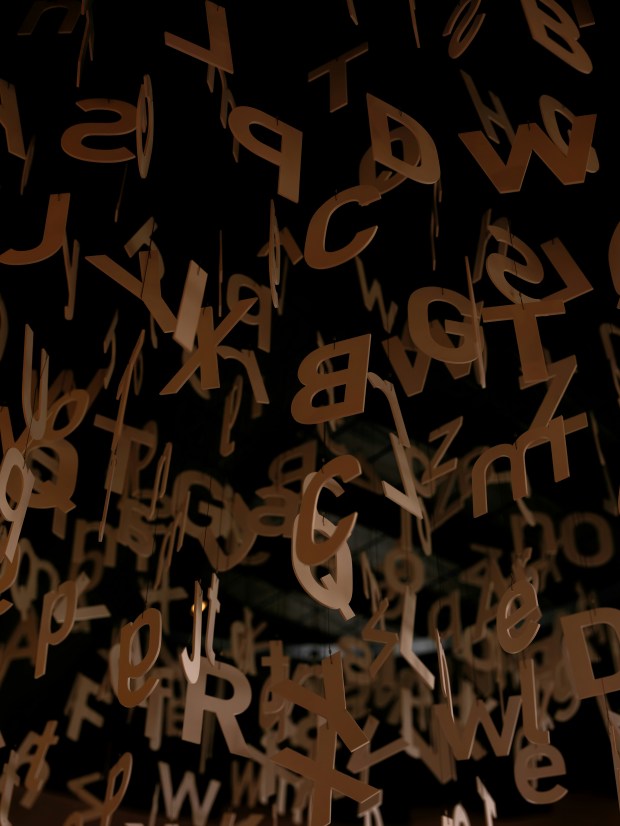Photo of cardboard upper and lower case letters hanging from the ceiling in a dark room.