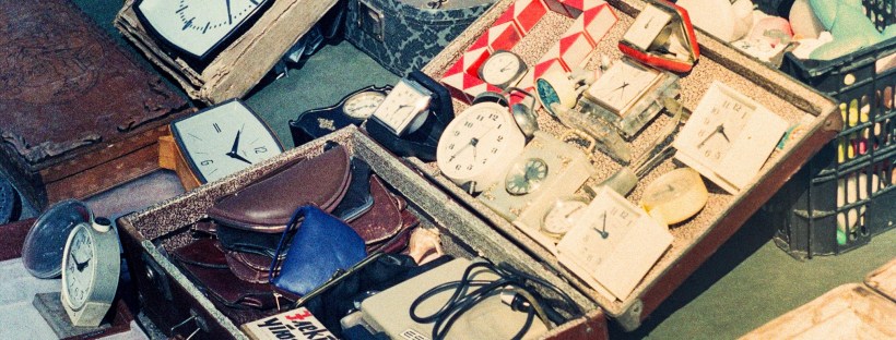 Grainy photo of open suitcases at a flea market, containing clocks, trinkets, and photos.