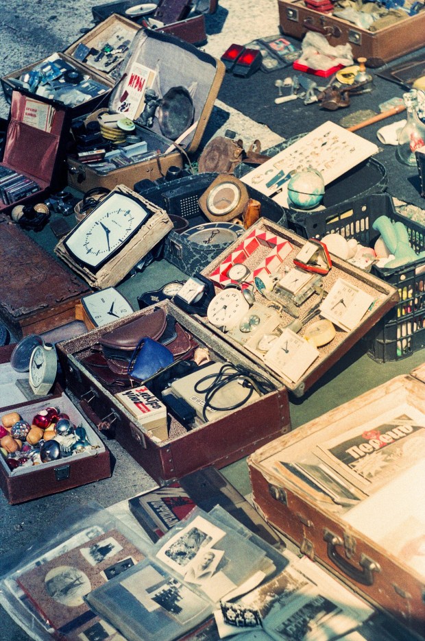 Grainy photo of open suitcases at a flea market, containing clocks, trinkets, and photos.