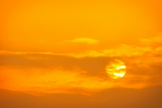 Photo of the sun in an orange sky with sparse clouds.