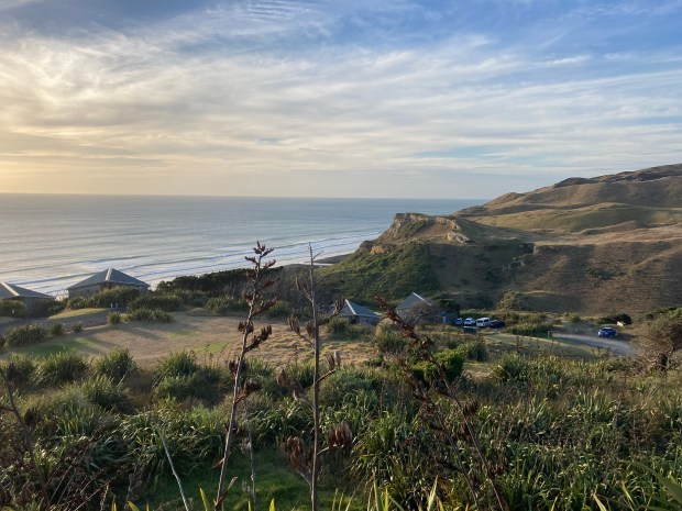 Photo overlooking a valley of hills, green foliage, houses and cars, with a blue sea and sky on the horizon.
